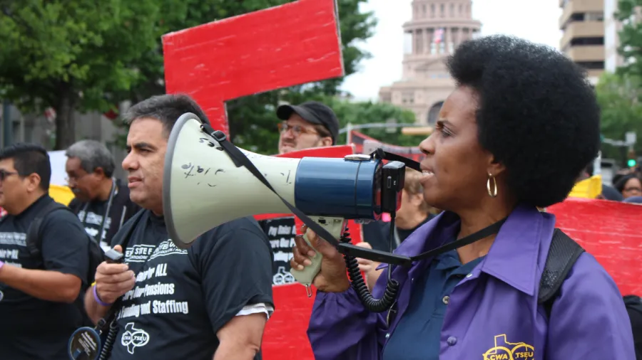 TSEU member speaks into a microphone in front of the Texas Capitol.